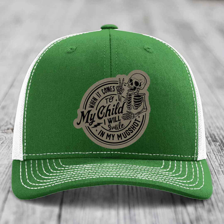Green trucker hat with white mesh back and stitching, featuring a circular patch with skeleton graphic and text: &