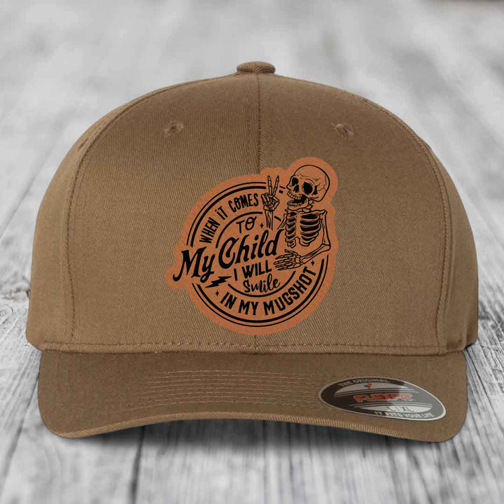 Tan baseball cap with a brown leatherette patch featuring a skeleton holding up two fingers and the text &
