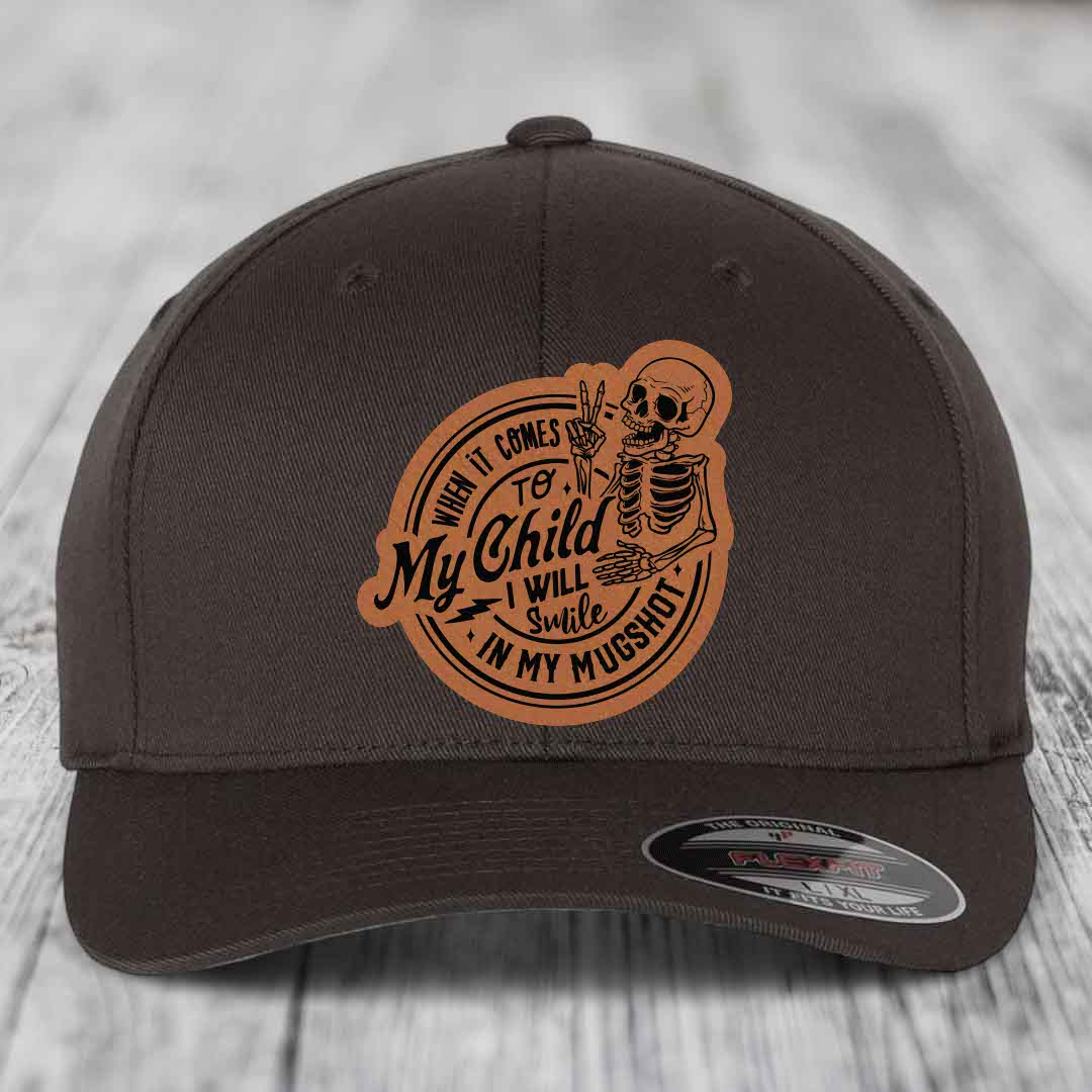 Dark brown baseball cap with a tan leatherette patch featuring a skeleton holding a peace sign and the text &