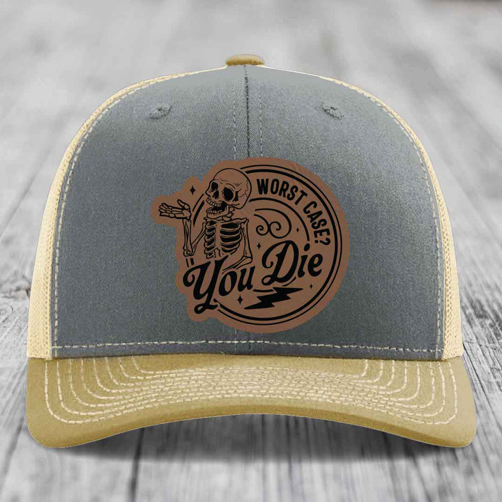 Grey and beige trucker hat with a brown leather patch featuring a skeleton and the text &