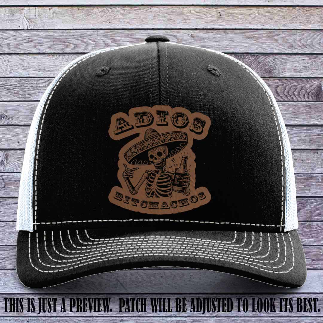 Dark brown leather patch on Black to White Richardson 112 trucker hat featuring “Adios Bitchachos” skeleton design.