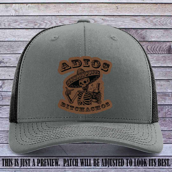 Dark brown leather patch on Heather Grey to Black Richardson 112 trucker hat featuring “Adios Bitchachos” skeleton design.