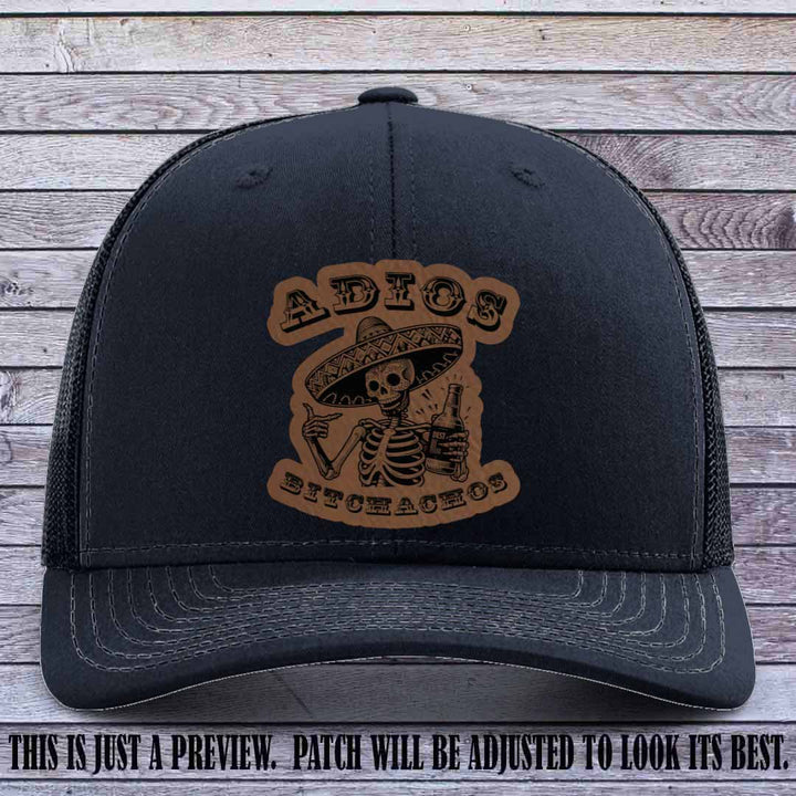 Dark brown leather patch on Navy Richardson 112 trucker hat featuring “Adios Bitchachos” skeleton design.