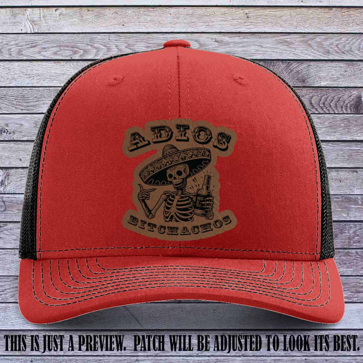 Dark brown leather patch on Red to Black Richardson 112 trucker hat featuring “Adios Bitchachos” skeleton design.
