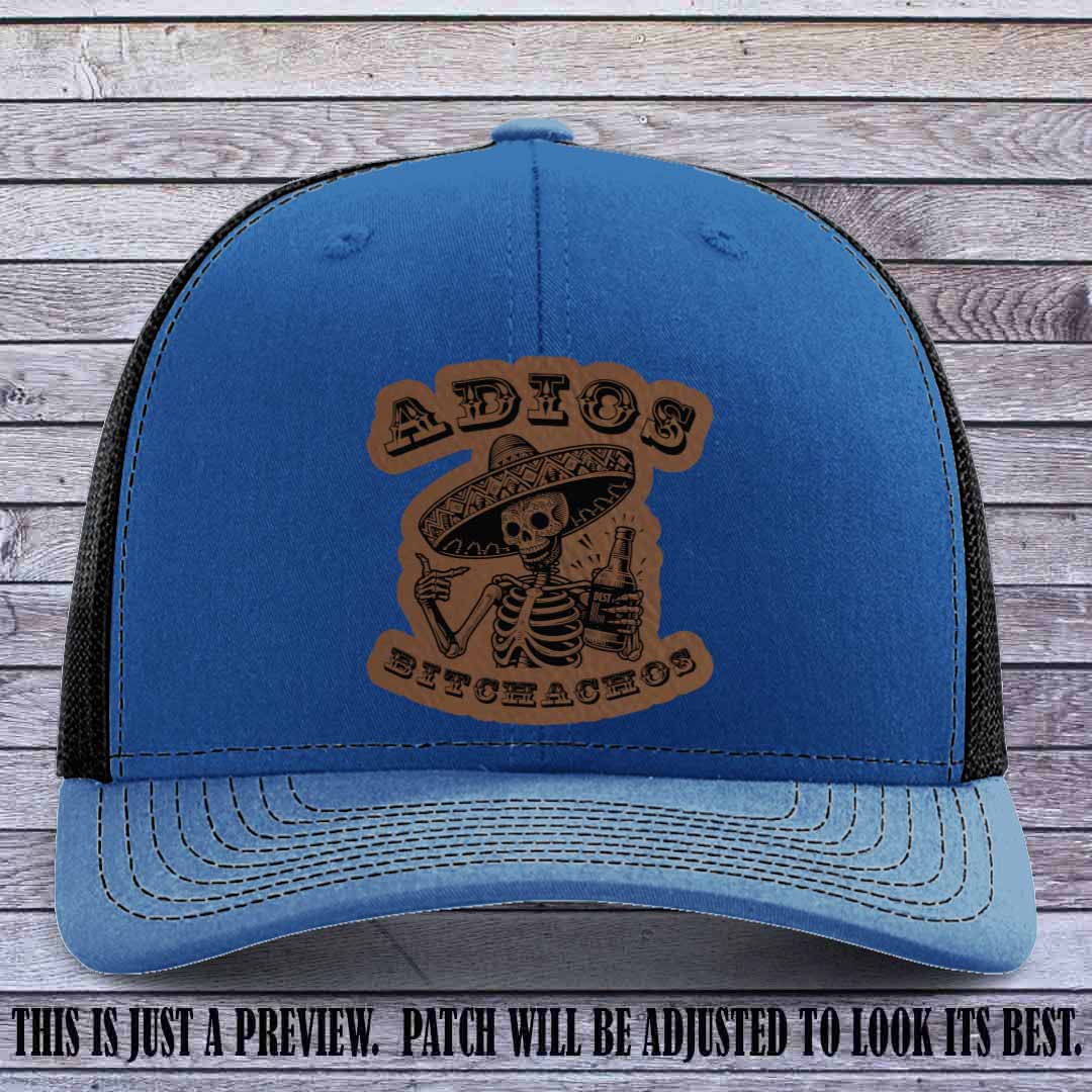 Dark brown leather patch on Royal to Black Richardson 112 trucker hat featuring “Adios Bitchachos” skeleton design.