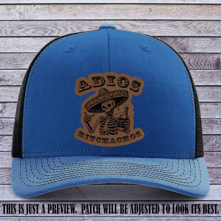 Dark brown leather patch on Royal to Black Richardson 112 trucker hat featuring “Adios Bitchachos” skeleton design.