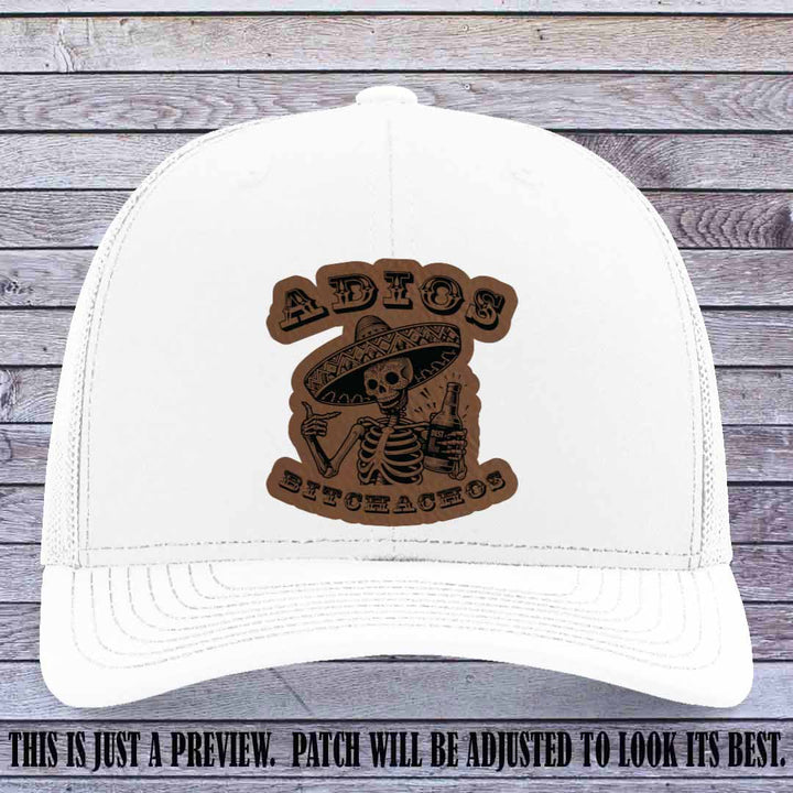 Dark brown leather patch on White Richardson 112 trucker hat featuring “Adios Bitchachos” skeleton design.