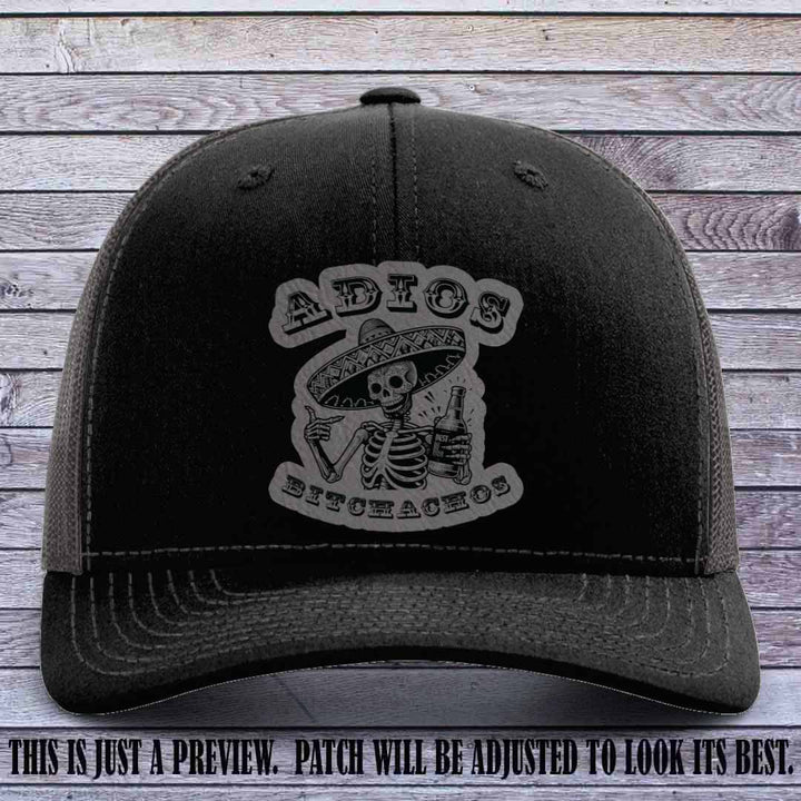 Grey leather patch on Black to Charcoal Richardson 112 trucker hat featuring “Adios Bitchachos” skeleton design.