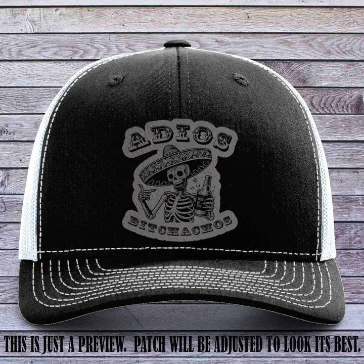 Grey leather patch on Black to White Richardson 112 trucker hat featuring “Adios Bitchachos” skeleton design.
