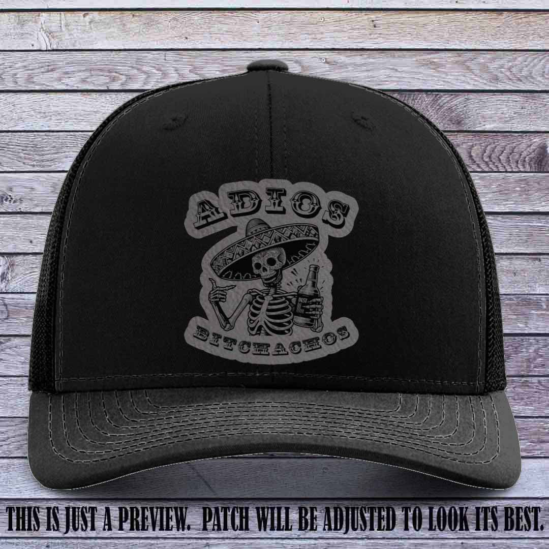 Grey leather patch on Black Richardson 112 trucker hat featuring “Adios Bitchachos” skeleton design.