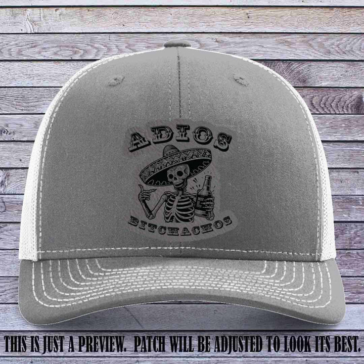 Grey leather patch on Heather Grey to White Richardson 112 trucker hat featuring “Adios Bitchachos” skeleton design.