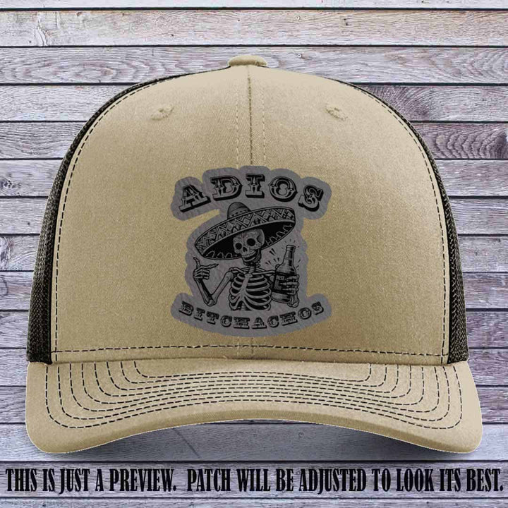 Grey leather patch on Khaki to Coffee Richardson 112 trucker hat featuring “Adios Bitchachos” skeleton design.