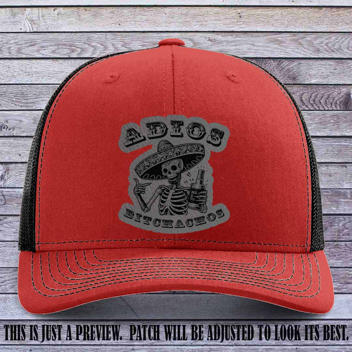 Grey leather patch on Red to Black Richardson 112 trucker hat featuring “Adios Bitchachos” skeleton design.
