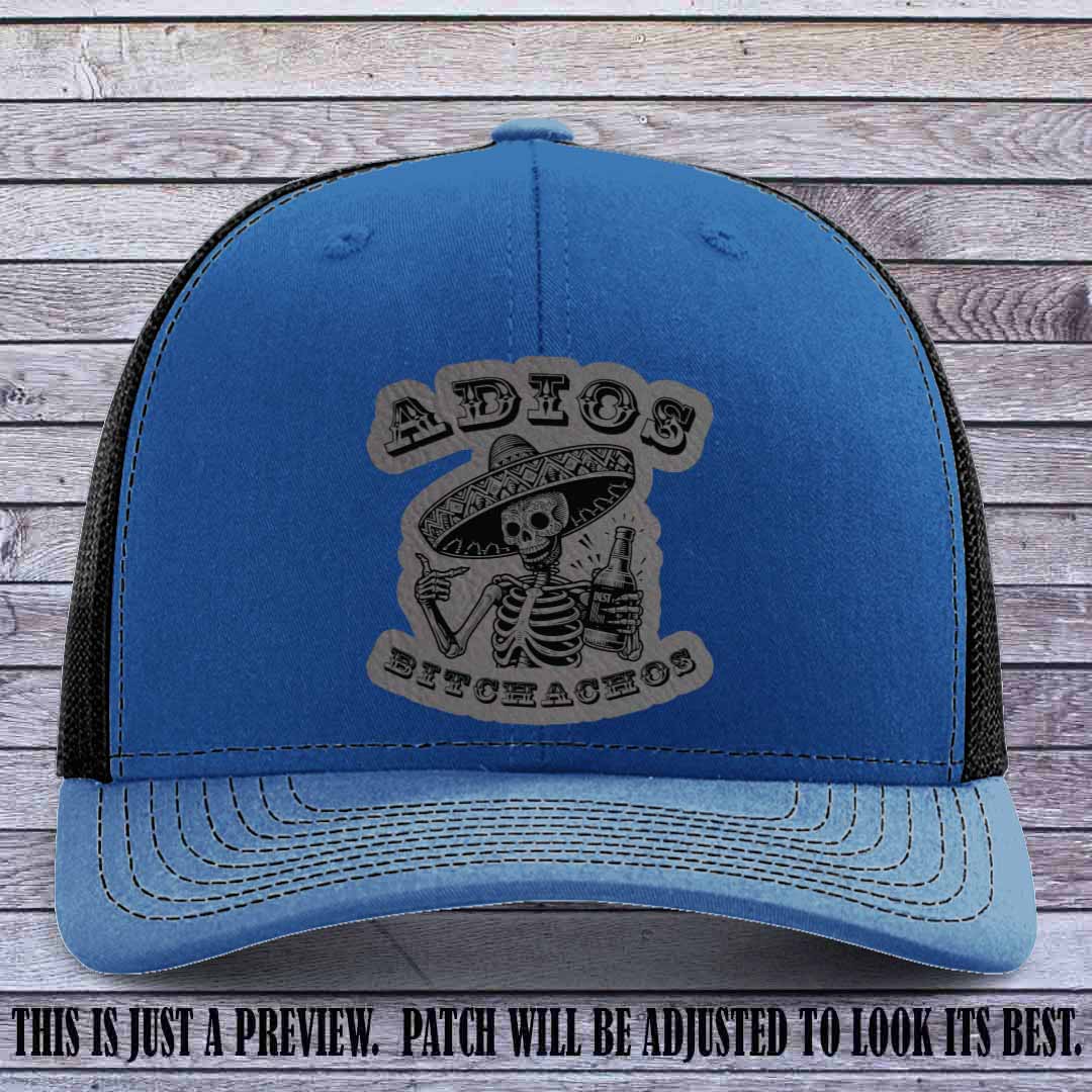 Grey leather patch on Royal to Black Richardson 112 trucker hat featuring “Adios Bitchachos” skeleton design.