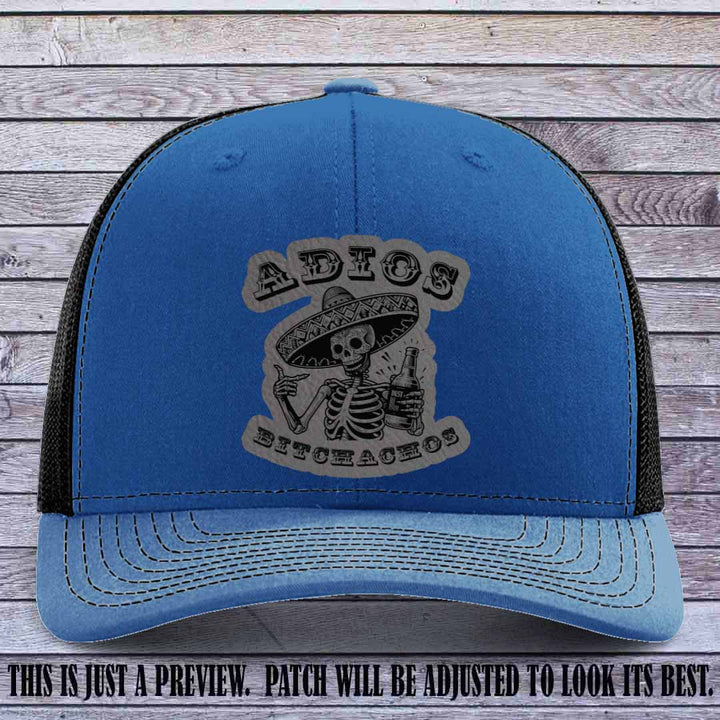 Grey leather patch on Royal to Black Richardson 112 trucker hat featuring “Adios Bitchachos” skeleton design.