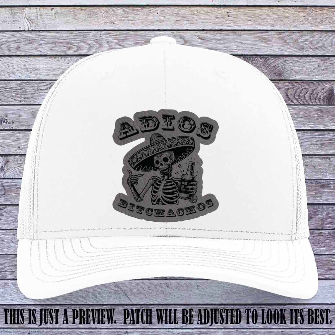 Grey leather patch on White Richardson 112 trucker hat featuring “Adios Bitchachos” skeleton design.