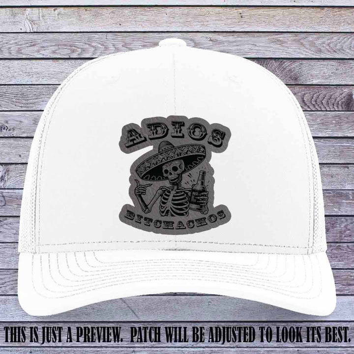 Grey leather patch on White Richardson 112 trucker hat featuring “Adios Bitchachos” skeleton design.