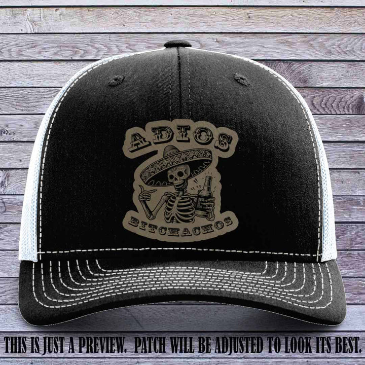 Light brown leather patch on Black to White Richardson 112 trucker hat featuring “Adios Bitchachos” skeleton design.