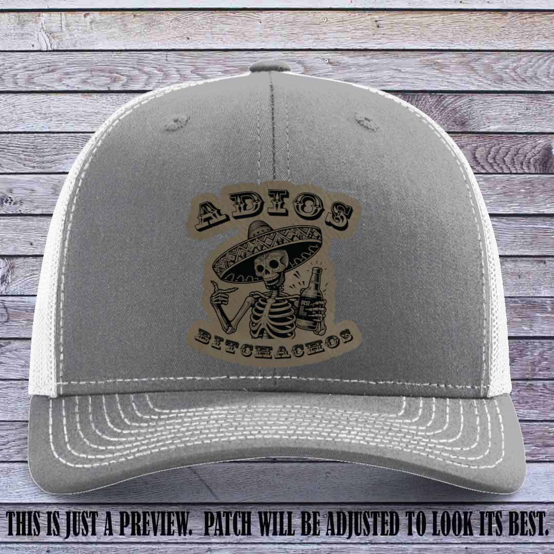 Light brown leather patch on Heather Grey to White Richardson 112 trucker hat featuring “Adios Bitchachos” skeleton design.