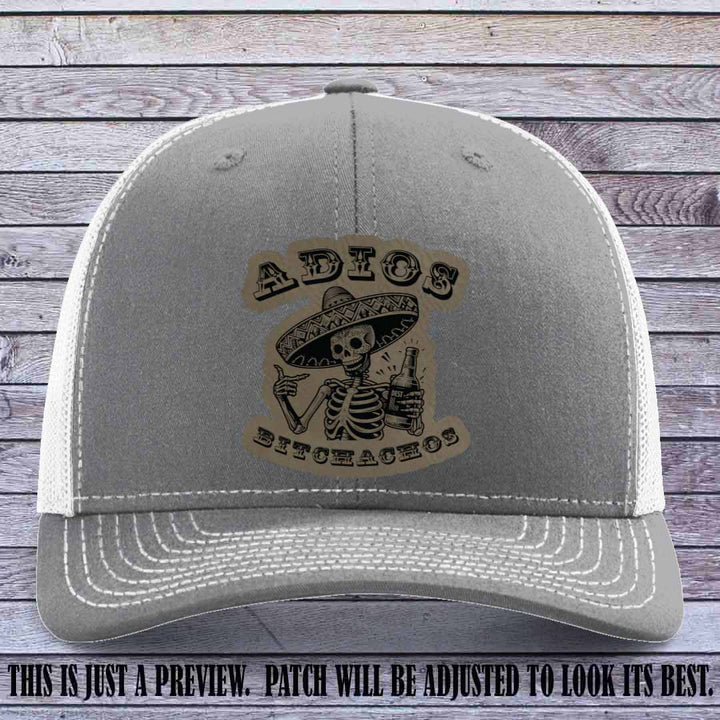 Light brown leather patch on Heather Grey to White Richardson 112 trucker hat featuring “Adios Bitchachos” skeleton design.
