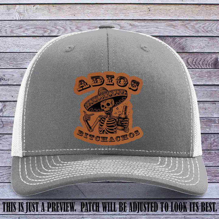 Rawhide leather patch on Heather Grey to White Richardson 112 trucker hat featuring “Adios Bitchachos” skeleton design.